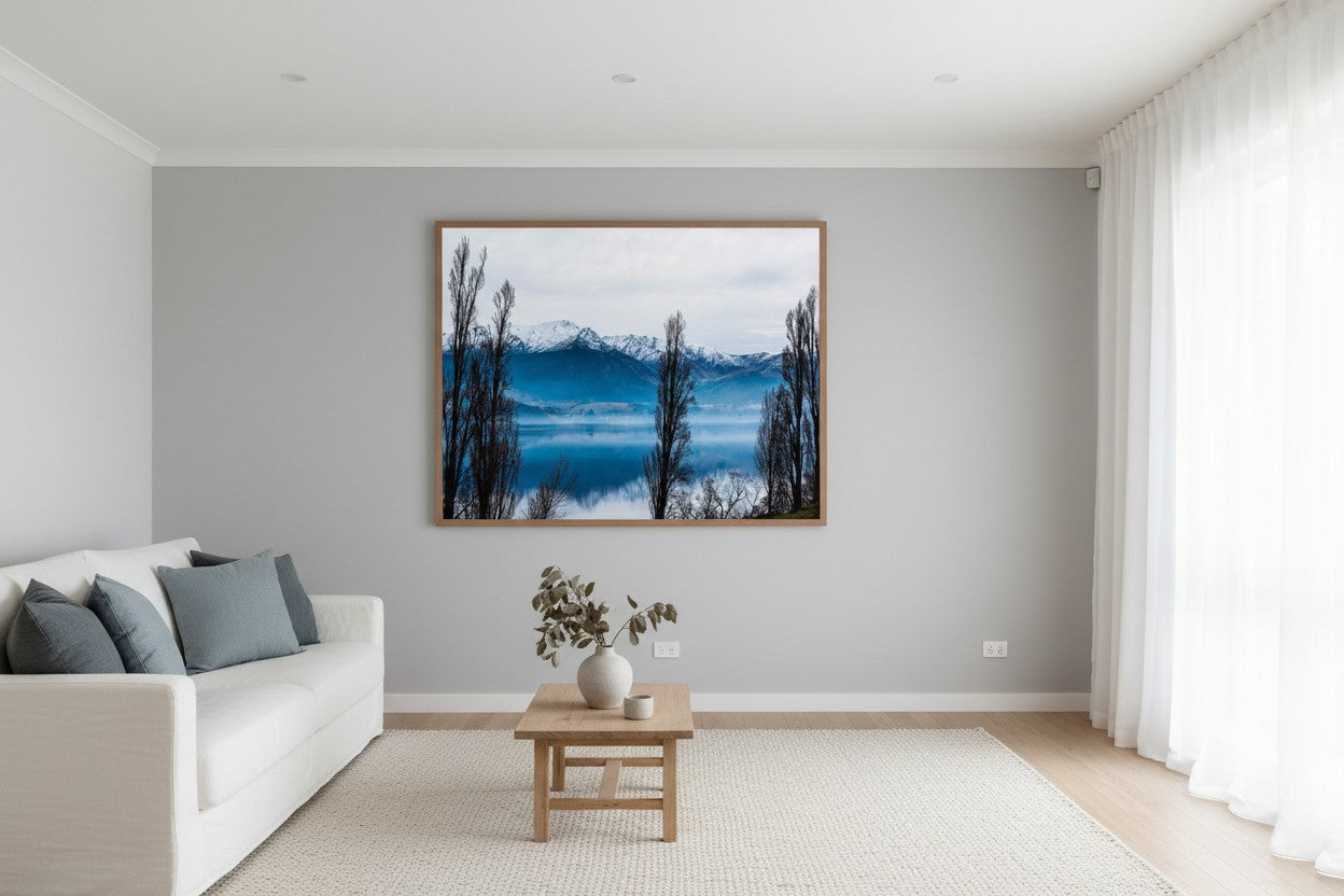 Lake Hayes fine art print in a thin timber frame above a white linen sofa in a bright calm Australian living room — unframed New Zealand landscape wall art