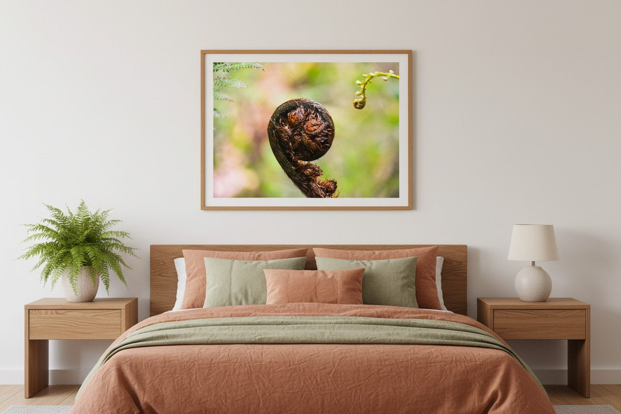 Begin botanical fine art print in a thin timber frame above a bed in a calm earthy bedroom with warm linen and indoor plants — unframed fern wall art
