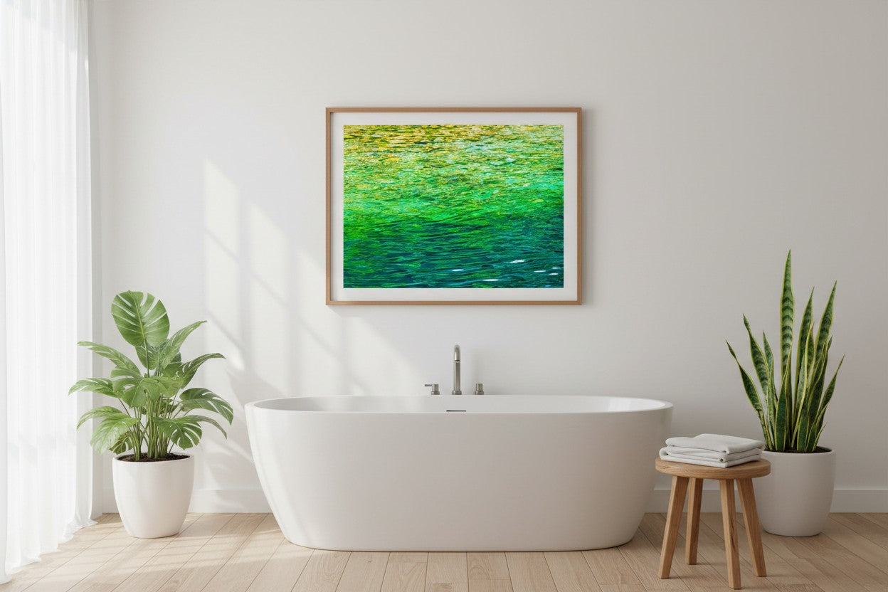 Crystal Creek fine art print in a thin timber frame above a freestanding bathtub in a bright spa-style bathroom with timber accents and green plants — unframed wall art