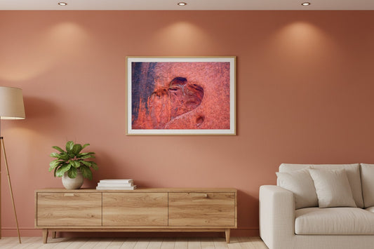 Heart of Uluṟu fine art print in a thin timber frame on a warm terracotta feature wall in a sophisticated contemporary living room — unframed Australian rock art wall print