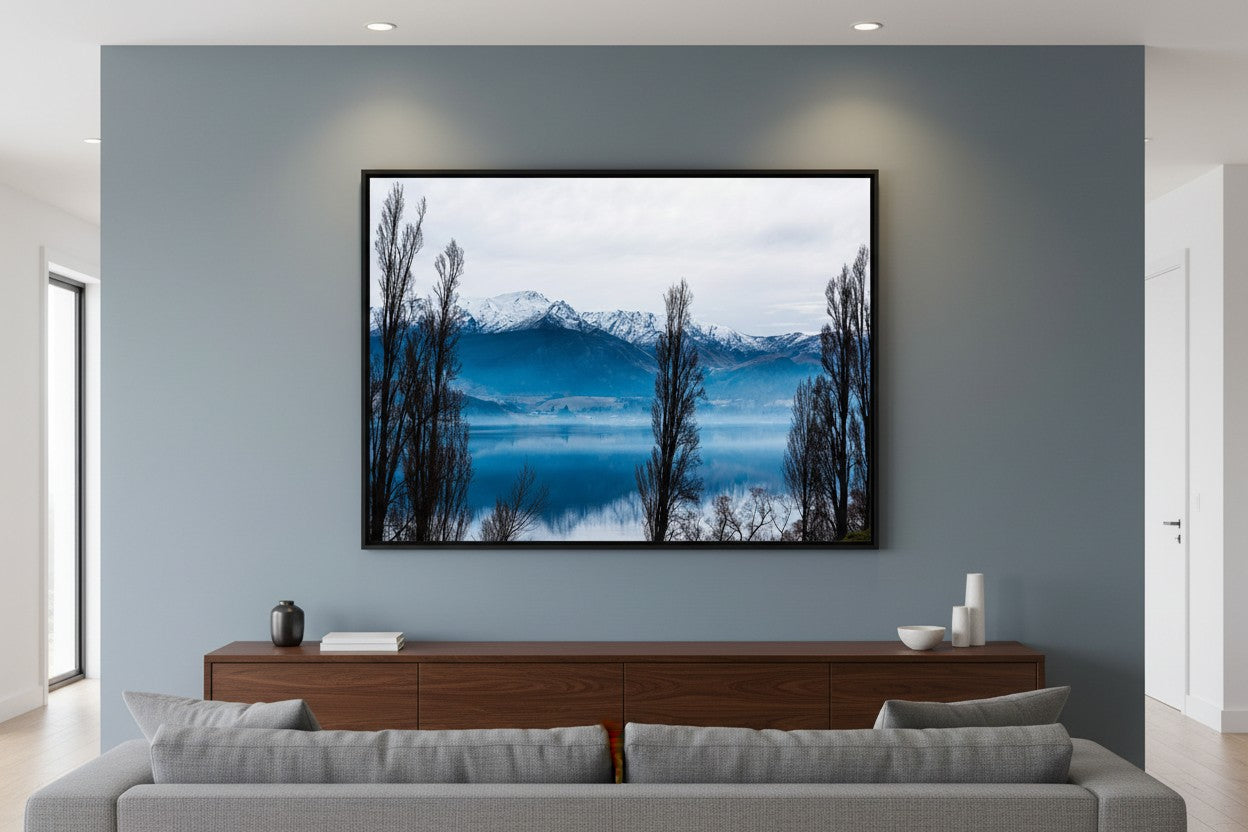 Lake Hayes fine art print in a thin black frame on a slate blue feature wall in a sophisticated contemporary living room — unframed New Zealand landscape wall art