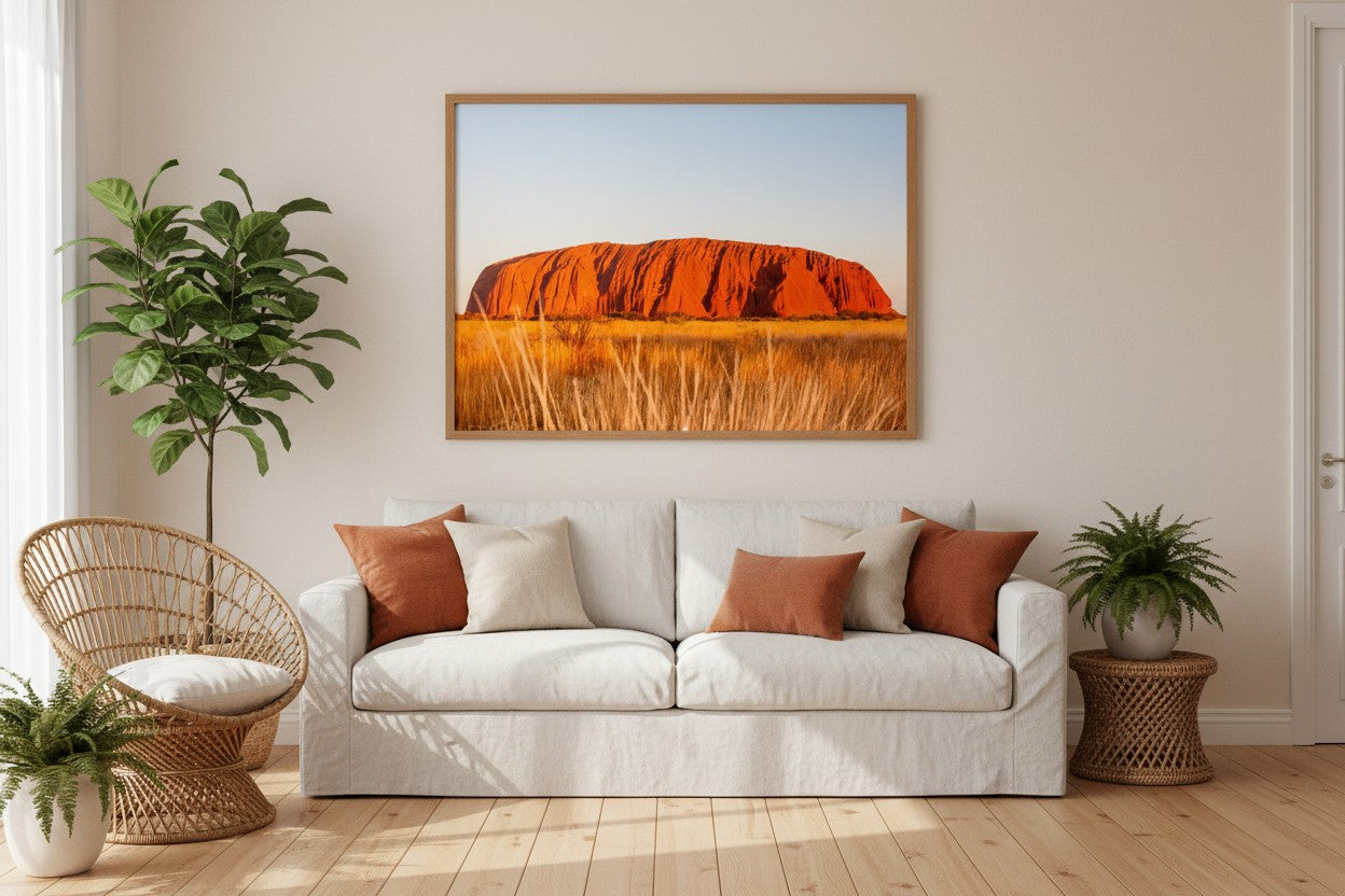 Uluṟu fine art print in a thin timber frame above a white linen sofa in a bright Australian living room with terracotta and rattan accents — unframed wall art