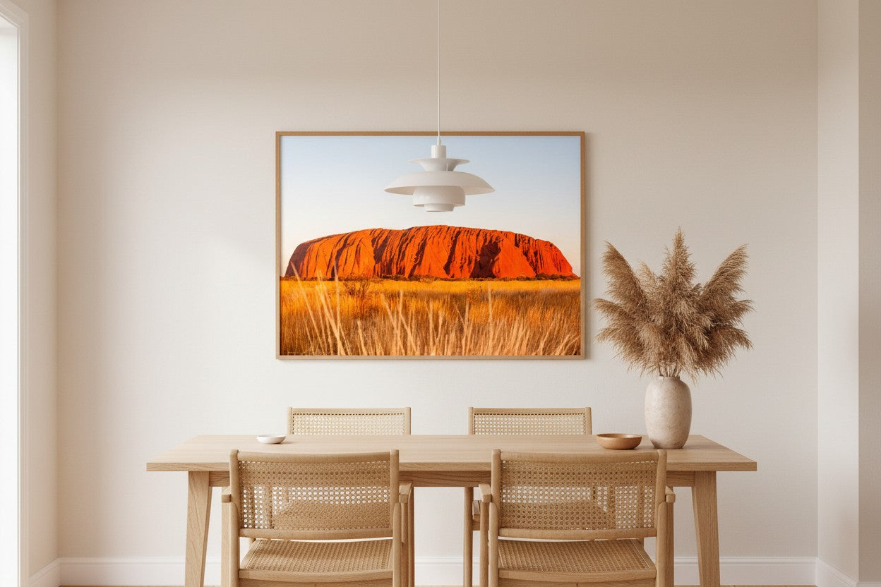 Uluṟu fine art print in a thin timber frame in a bright minimalist dining room with rattan chairs and dried pampas grass — unframed Australian wall art