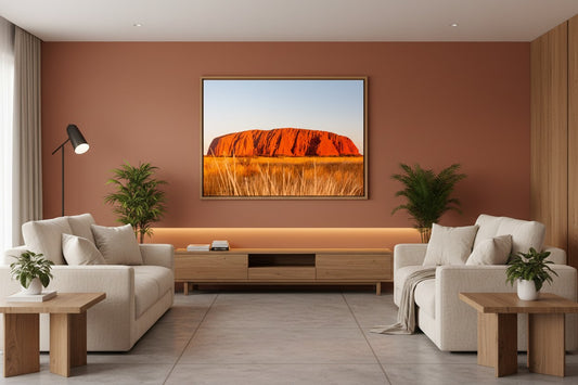 Uluṟu fine art print in a thin timber frame on a warm terracotta feature wall in a sophisticated contemporary living room — unframed Australian landscape wall art